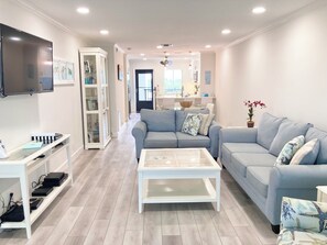 A modern living room with a sofa, coffee table, and a TV mounted on the wall. - Sunrise Cove 303: Remodeled Waterfront Condo on Siesta Key w/ 2 Sleeper Sofas (Sarasota)