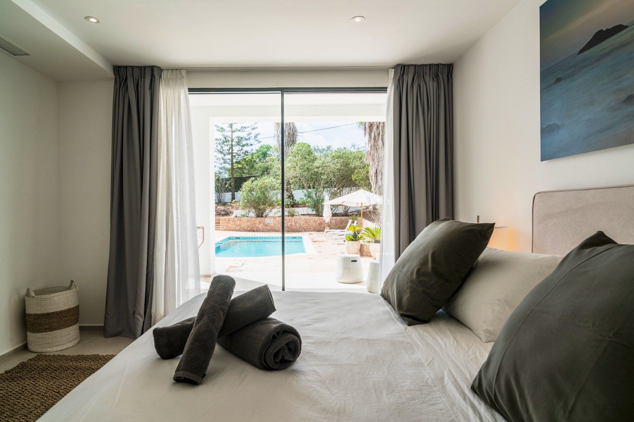 A hotel room with a bed, a view of an outdoor swimming pool, and a painting on the wall.
