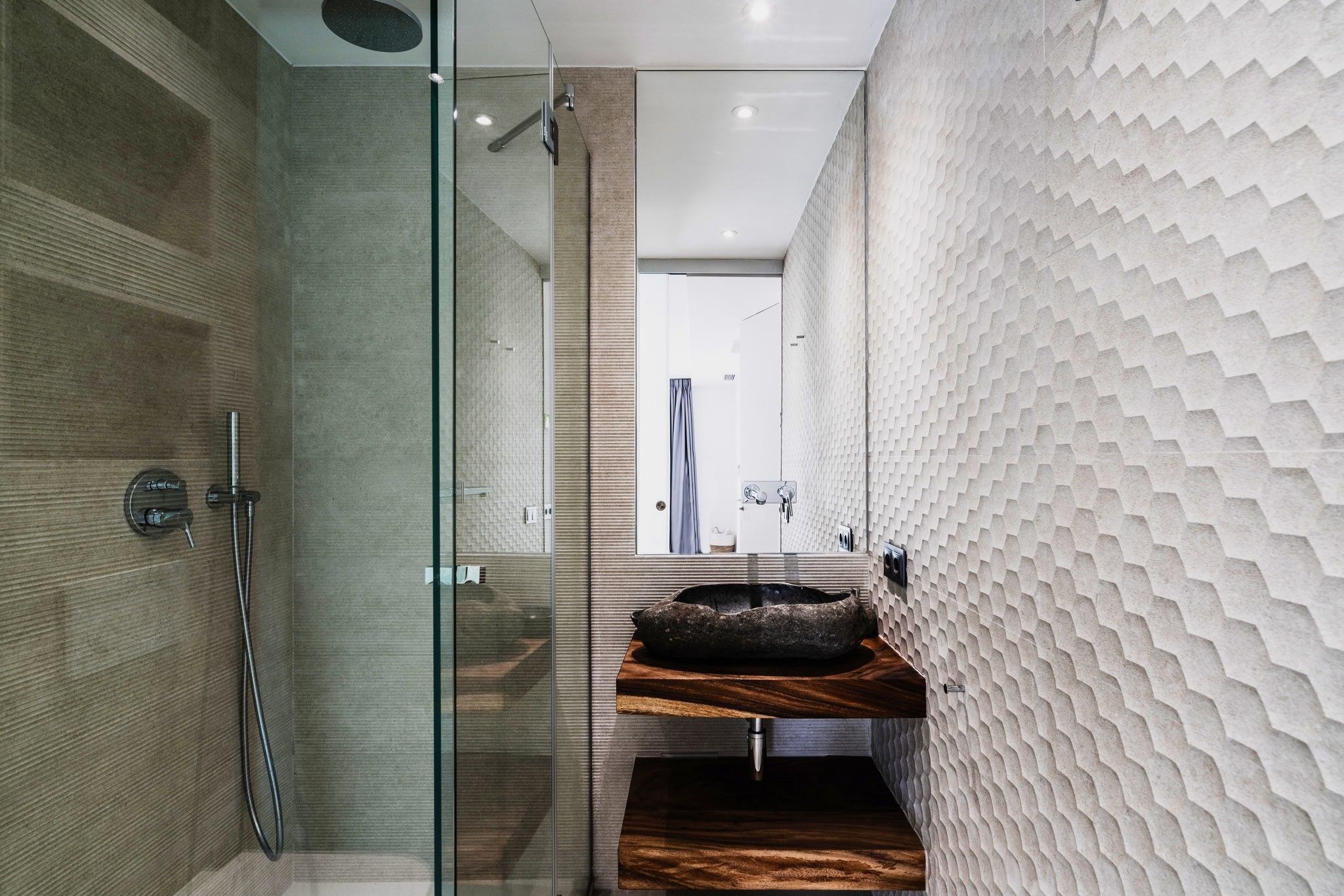 A modern bathroom with a glass shower enclosure, a wooden vanity, and textured wall panels.