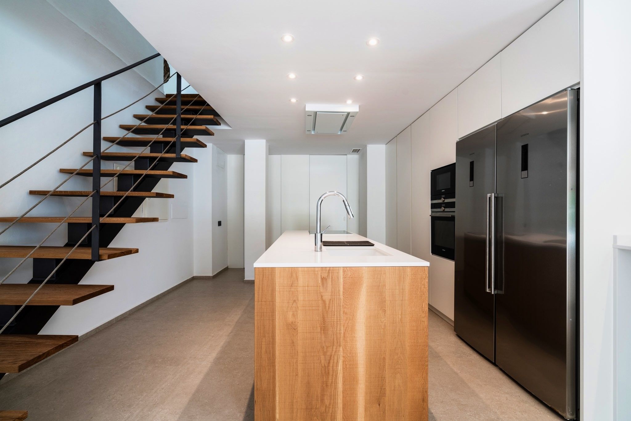 Una cocina moderna con una isla central, electrodomésticos de acero inoxidable y una escalera de madera.