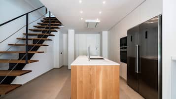 Una cocina moderna con una isla central, electrodomésticos de acero inoxidable y una escalera de madera.