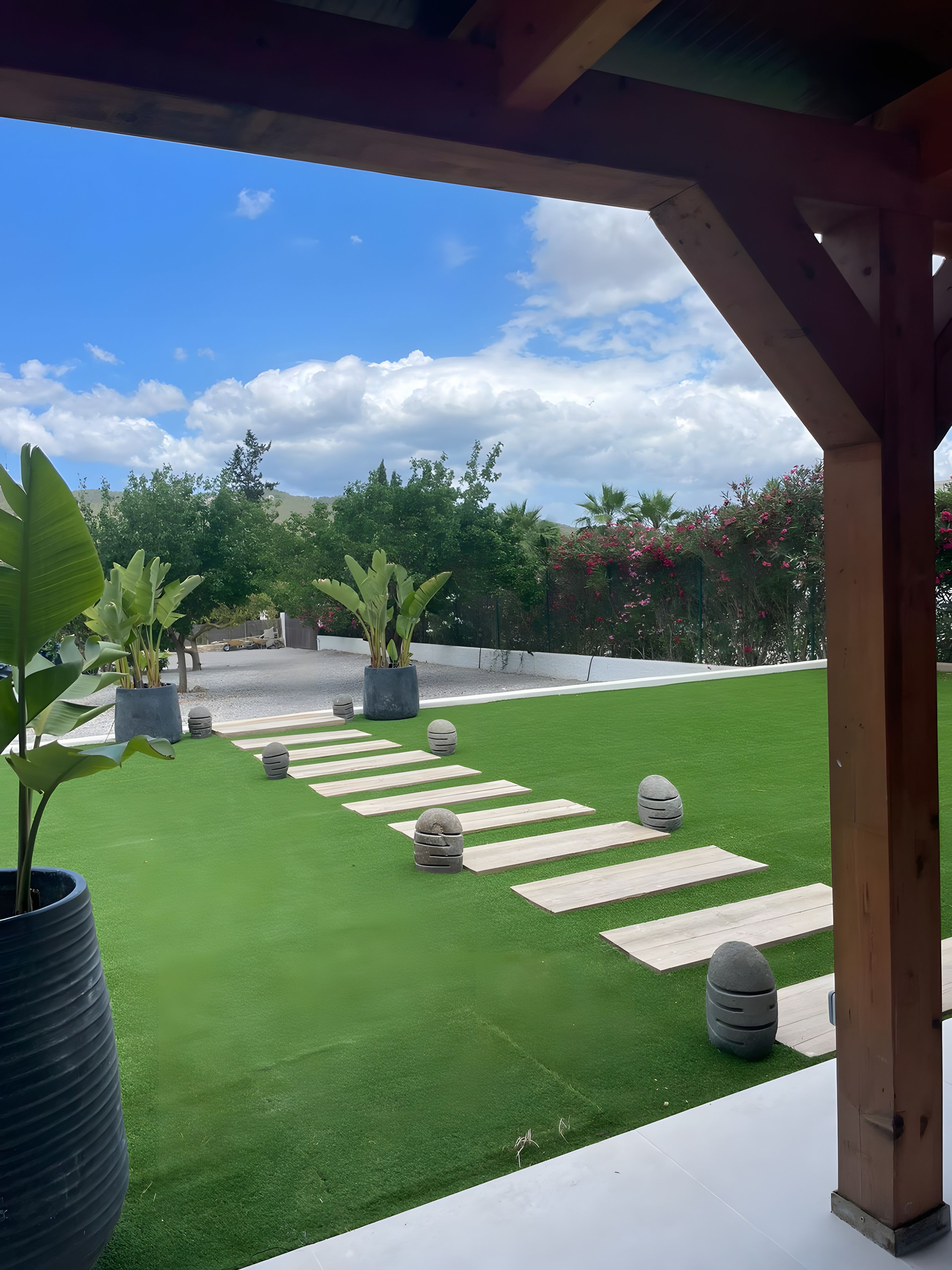 Un área de patio con césped artificial, plantas en macetas y una estructura de pérgola de madera.