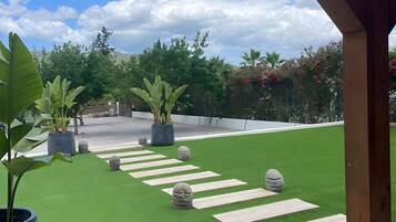 Un área de patio con césped artificial, plantas en macetas y una estructura de pérgola de madera.