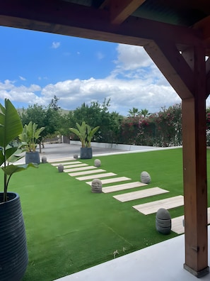 Zona de pati amb gespa artificial, plantes en testos i una estructura de pergola de fusta.