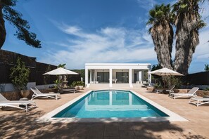 Zona de piscina moderna amb una piscina rectangular, gandules blanques i ombrelles.