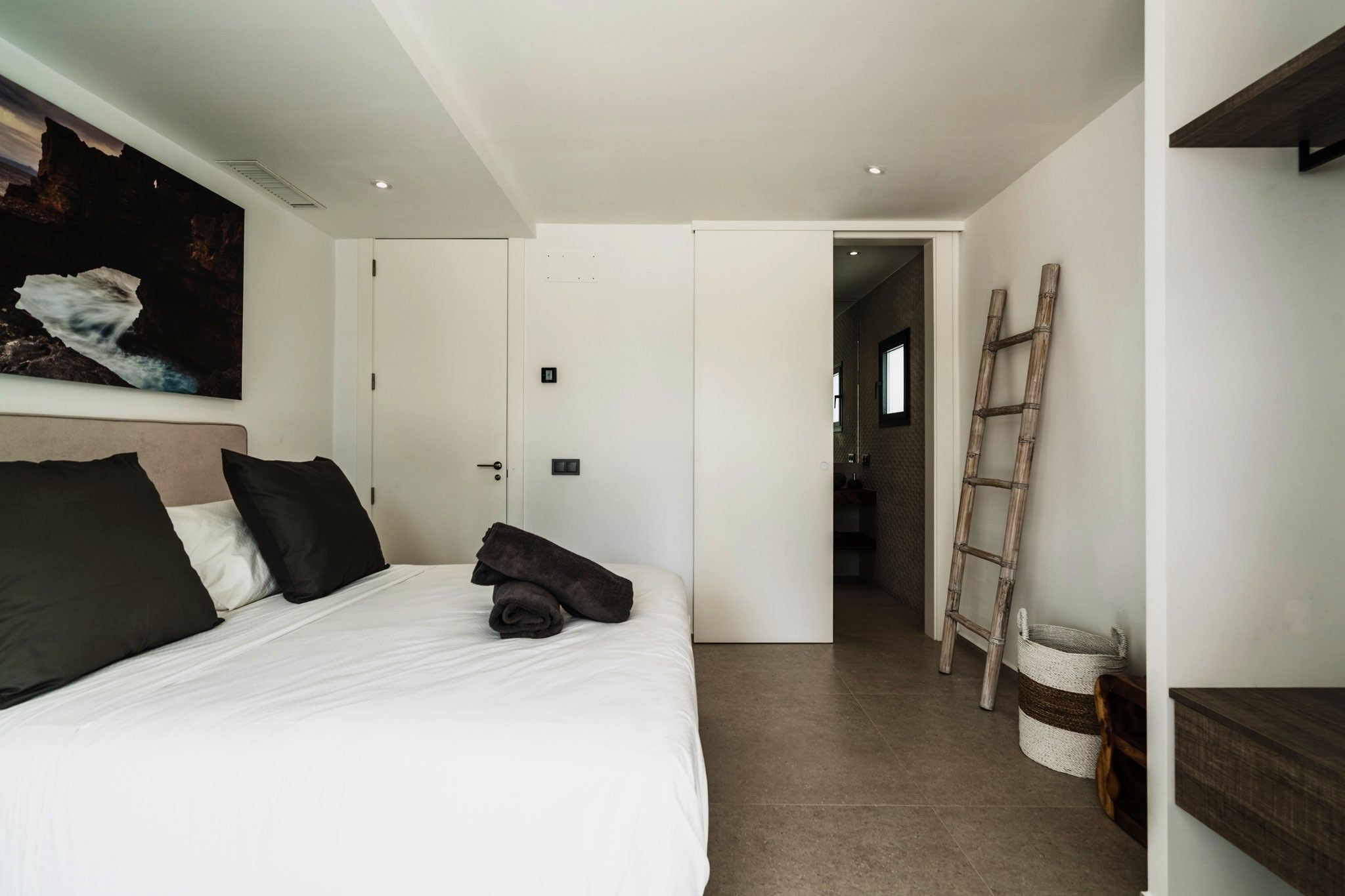 Un dormitorio con cama, una puerta, una escalera y un estante fijado a la pared.