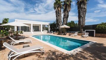 A swimming pool with lounge chairs, a covered seating area, and tall palm trees.