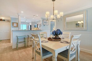 A dining area with a table set for four, surrounded by white chairs. A chandelier hangs above the table, and a mirror is mounted on the wall to the right. - Sunrise Cove 308: Remodeled Stunning Coastal Waterfront Condo on Siesta Key (Sarasota)