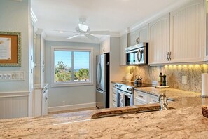 A kitchen with white cabinetry, a microwave, a refrigerator, and a ceiling fan. - Sunrise Cove 308: Remodeled Stunning Coastal Waterfront Condo on Siesta Key (Sarasota)
