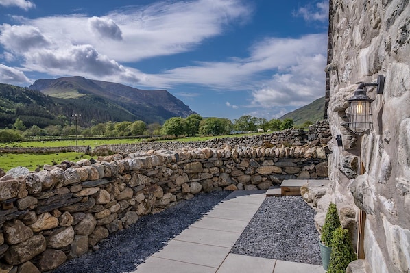 A stone wall leading to a building with a stone pathway and a mountain view in the background.
