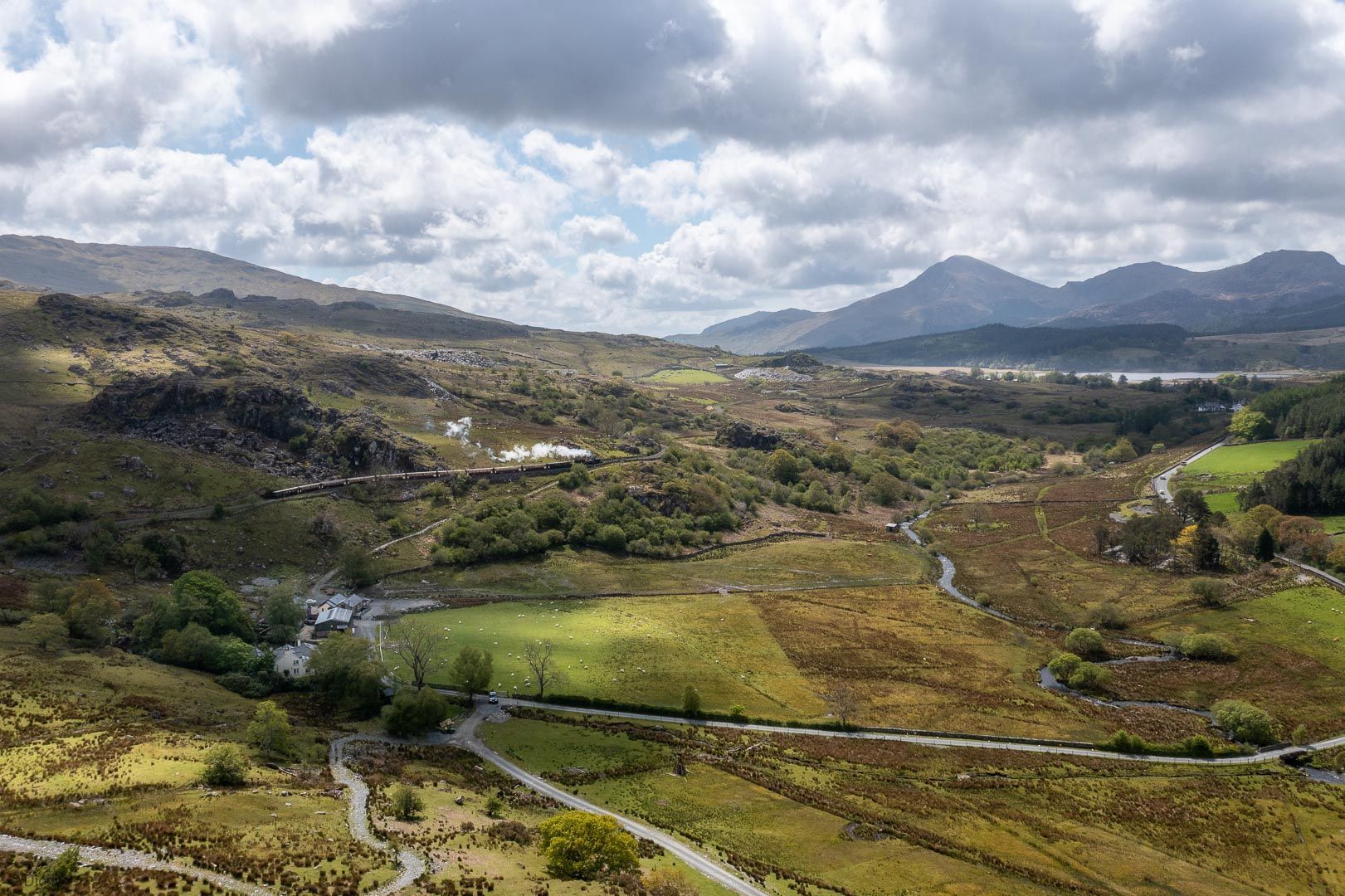 A rural landscape with a winding road, fields, and distant mountains.