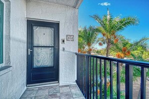 Ein Gebäude mit einer schwarzen Tür, einem Balkon mit Metallgeländer und einer Palme im Hintergrund.