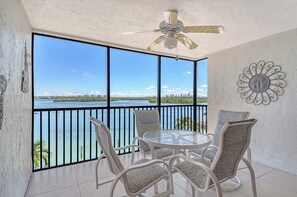 A balcony with a view of a body of water, a ceiling fan, and a round table with chairs. - Sunrise Cove 320: Remodeled Waterfront Condo on Siesta Key with Sleeper Sofa (Sarasota)