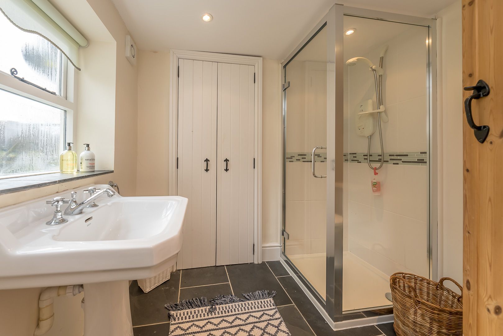 A bathroom with a white sink, a glass shower enclosure, and a wooden door.