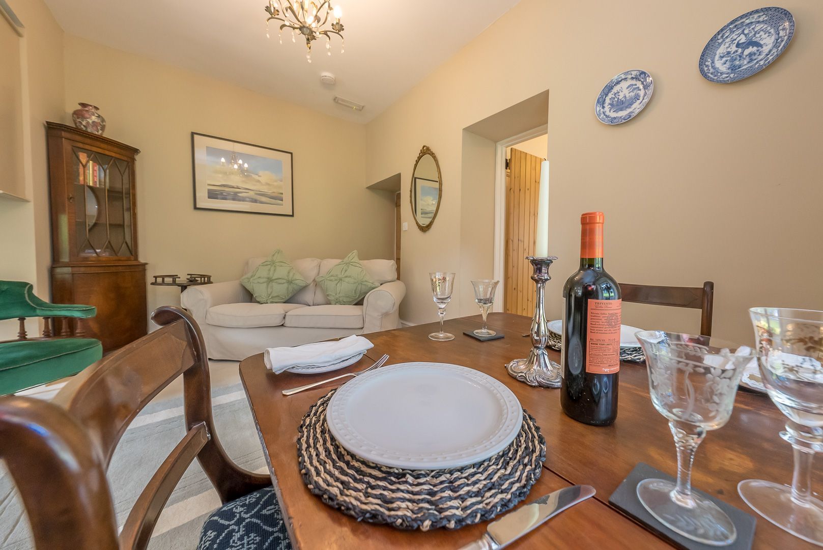 A dining room with a wooden table set for four, a sofa, a cabinet, and a chandelier.