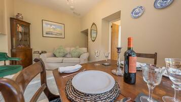 A dining room with a wooden table set for four, a sofa, a cabinet, and a chandelier.