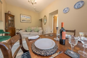 Une salle à manger avec une table en bois dressée pour quatre personnes, un canapé, un buffet et un lustre.