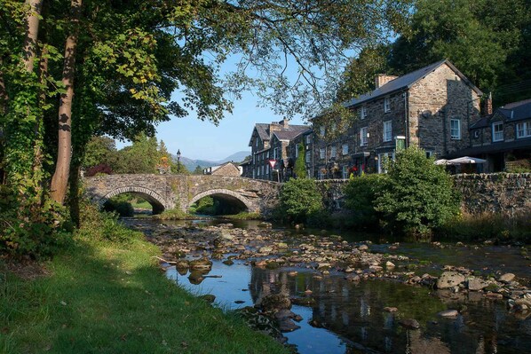 A stone bridge over a river, surrounded by lush greenery and traditional stone buildings.