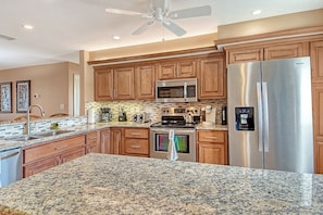 A modern kitchen with granite countertops, stainless steel appliances, wooden cabinets, and a ceiling fan. - Sunrise Cove 324: Spacious Fully Remodeled Waterfront Condo on Siesta Key (Sarasota)