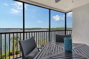 A balcony with a view of a body of water and distant buildings, furnished with a table and chairs. - Sunrise Cove 326: Remodeled Waterfront Vacation Rental Condo on Siesta Key (Sarasota)