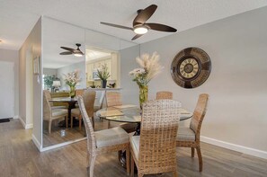 A dining area with wicker chairs, a glass table, and a ceiling fan. - Sunrise Cove 326: Remodeled Waterfront Vacation Rental Condo on Siesta Key (Sarasota)
