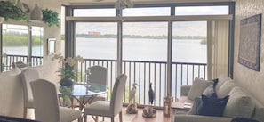 Ein Zimmer mit Balkon und Blick auf ein Gewässer, ausgestattet mit einer Couch, Sesseln und einem Tisch.
