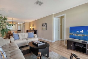 A living room with a sofa, coffee table, TV, and a plant. - Sunrise Cove 328: Remodeled Waterfront Condo on Siesta Key with Sleeper Sofa (Sarasota)