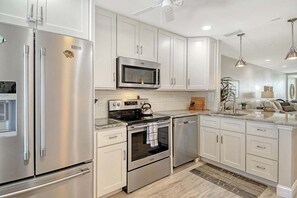 Une cuisine moderne dotée d’appareils électroménagers en acier inoxydable, de meubles blancs et d’un îlot central.