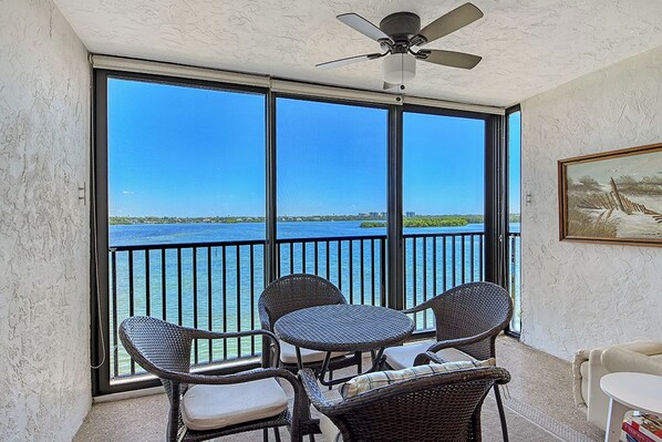 Ein Balkon mit Korbmöbeln, einem Deckenventilator und Blick auf das Wasser.