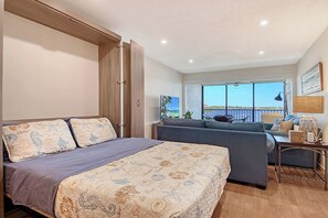 Ein Schlafzimmer mit einem Bett, einem Sofa, einem Schreibtisch und einem großen Fenster mit Blick.