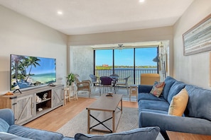 A living room with a TV, sofa, coffee table, and a balcony with a view. - Sunrise Cove 411: Modern Waterfront Condo on Siesta Key with Murphy Bed (Sarasota)