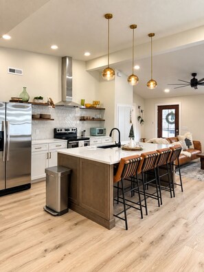 Cozinha moderna com ilha central, eletrodomésticos de aço inoxidável e iluminação pendente.