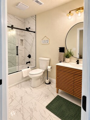 Ein Badezimmer mit Glasdusche, Toilette, Waschbecken mit Spiegel und einer grünen Matte auf dem Boden.