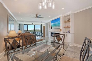 A modern living room with a glass coffee table, a fireplace, a large TV, and a balcony with a view. - Sunrise Cove 418: Remodeled Waterfront Condo on Siesta Key w/ Sleeper Sofa (Siesta Key)