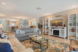 A living room with a sofa, coffee table, and a fireplace. There is a bookshelf and a TV mounted on the wall. - Sunrise Cove 425: Spacious Waterfront Condo on Siesta Key with Sleeper Sofa (Sarasota)