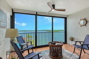 A balcony with a view of the sea, a ceiling fan, and a round table with chairs. - Sunrise Cove 506: Waterfront Kid Friendly Condo on Siesta Key w/ Sleeper Sofa (Sarasota)