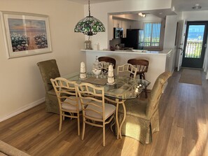 A dining area with a glass table, wooden chairs, and a decorative lamp. - Sunrise Cove 523: Waterfront Siesta Key Monthly Rental with Sleeper Sofa (Sarasota)