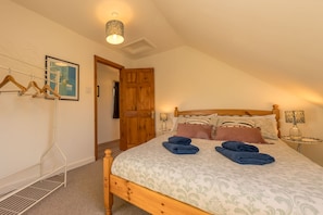 Un dormitorio con una cama de madera, una lámpara colgante, una puerta y un perchero en la pared.