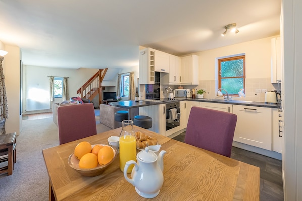 A modern kitchen with white cabinets, a dining area with a wooden table, and a staircase leading to another level.
