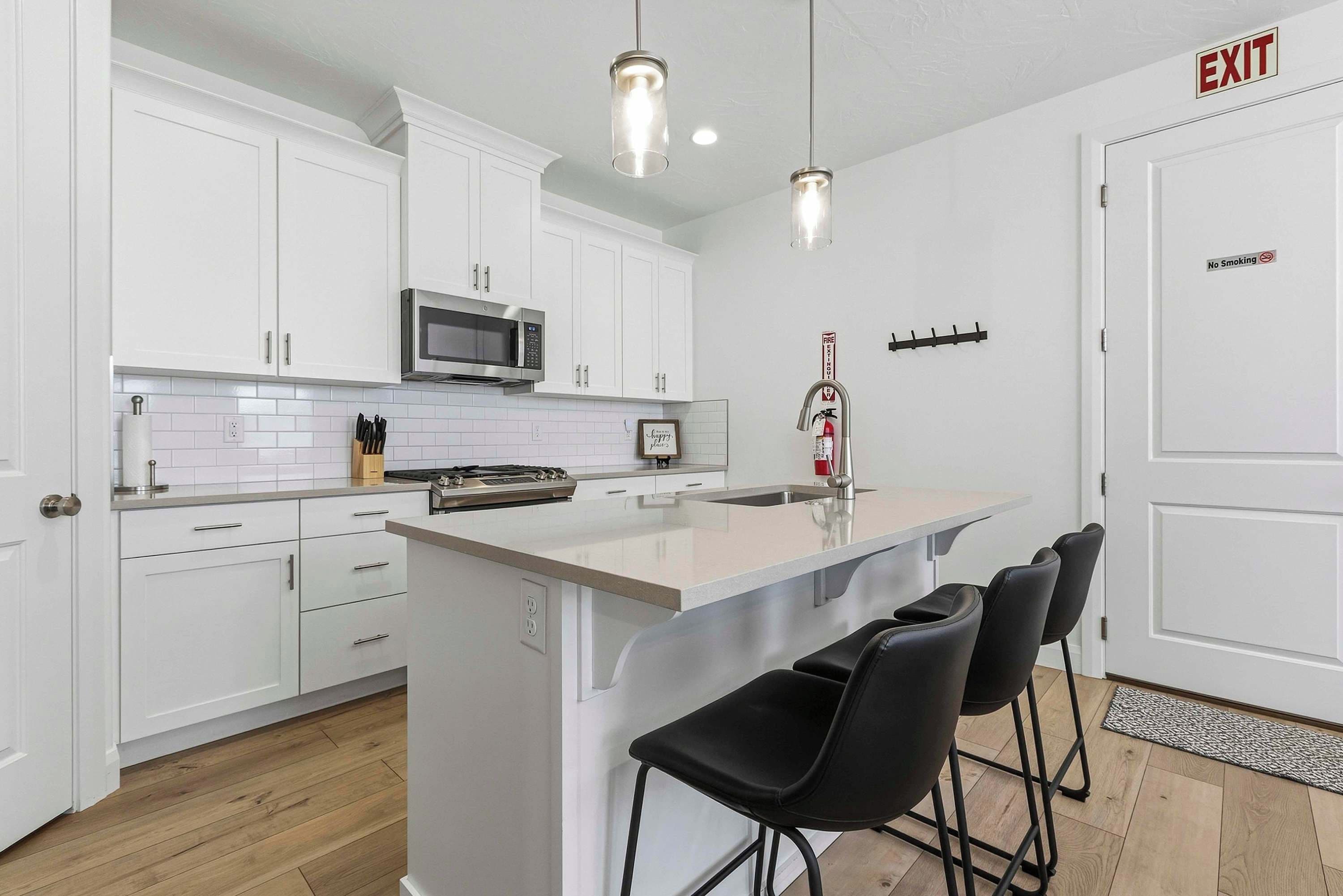 A modern kitchen with white cabinets, a central island with bar stools, a microwave, and a fire extinguisher.