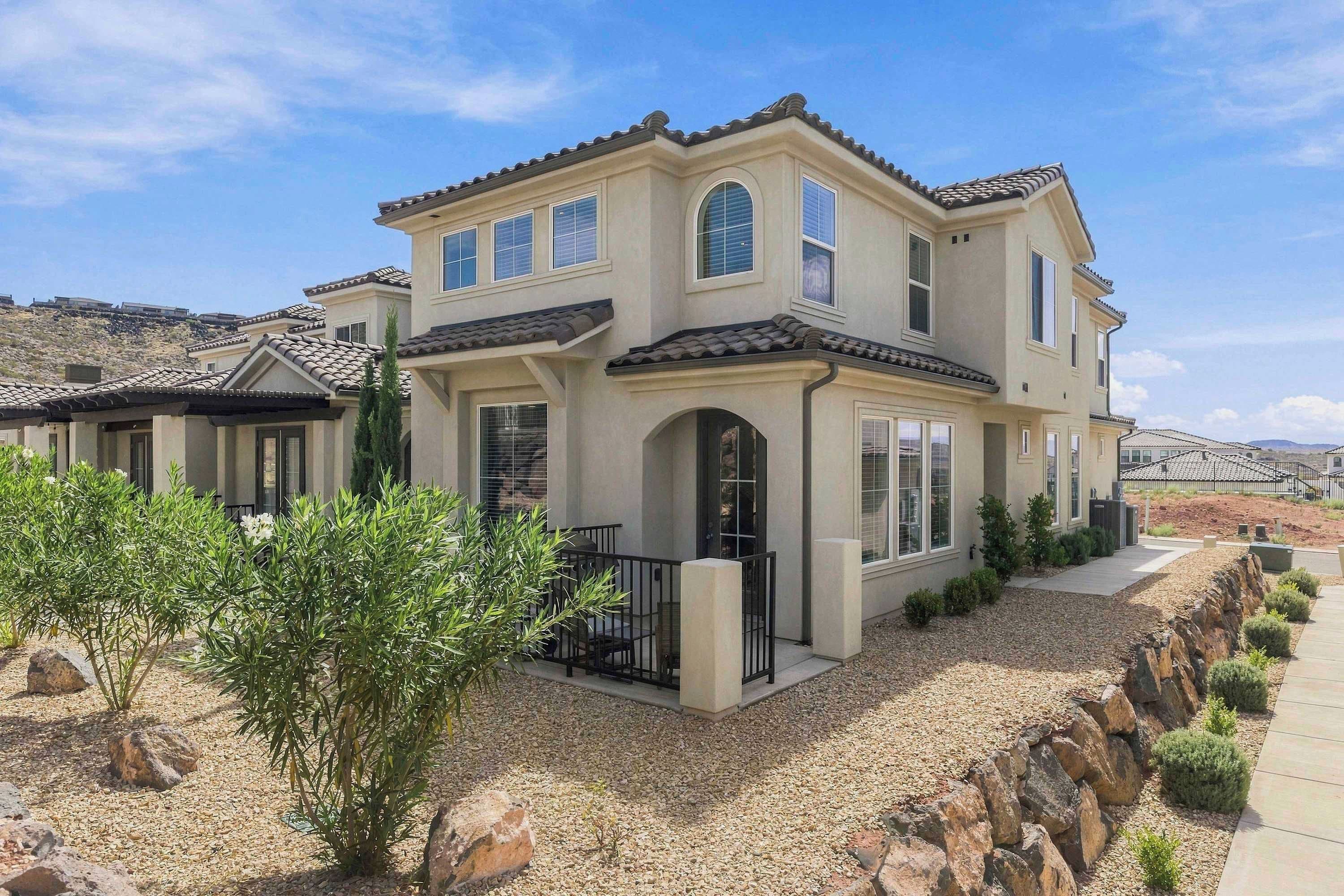 A two-story house with a patio, a small garden, and a view of the surrounding landscape.