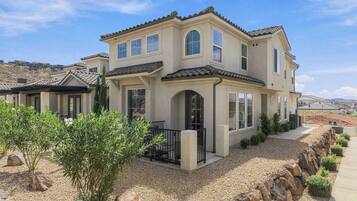 A two-story house with a patio, a small garden, and a view of the surrounding landscape.