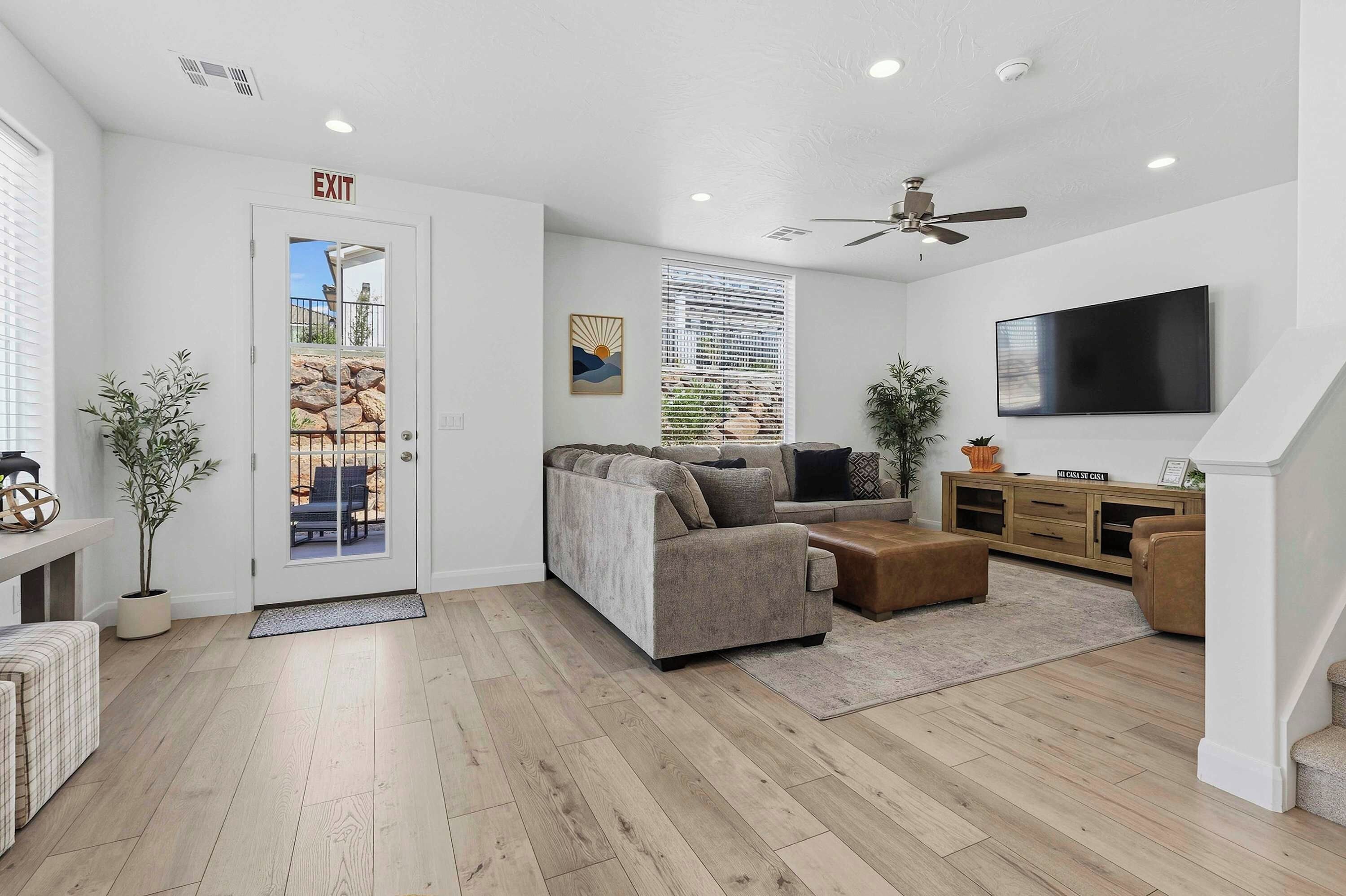 A modern living room with a sofa, ottoman, and a flat-screen TV.