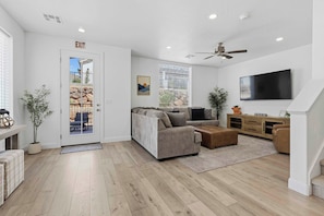 A modern living room with a sofa, ottoman, and a flat-screen TV.