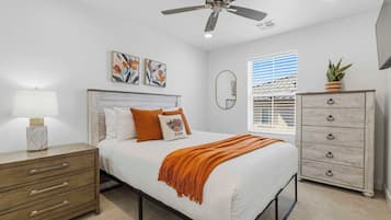 A bedroom with a bed, a nightstand, a dresser, a ceiling fan, and artwork on the wall.