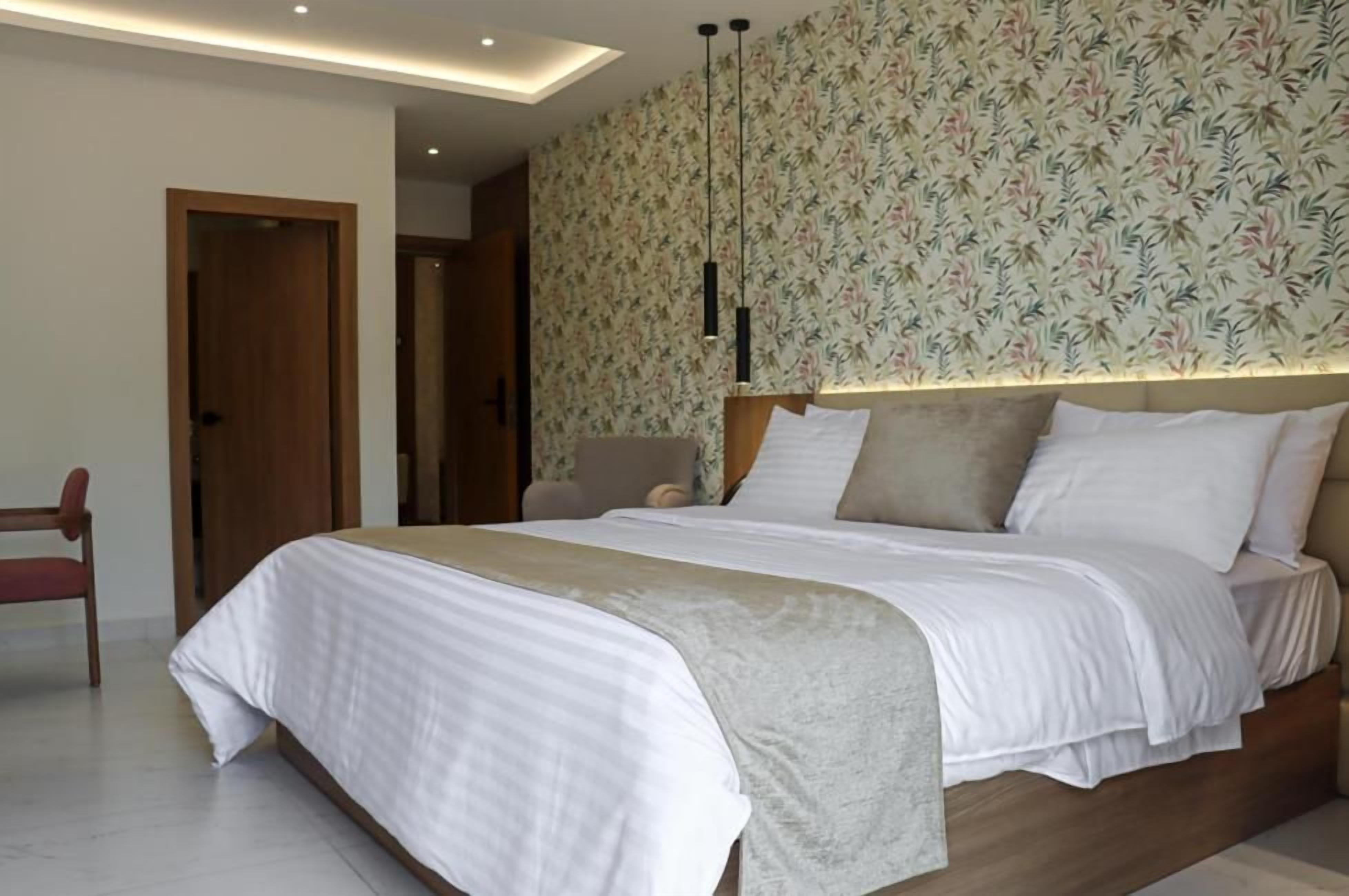 Un dormitorio con una cama, cabecera de madera, pared con estampado floral y una puerta.