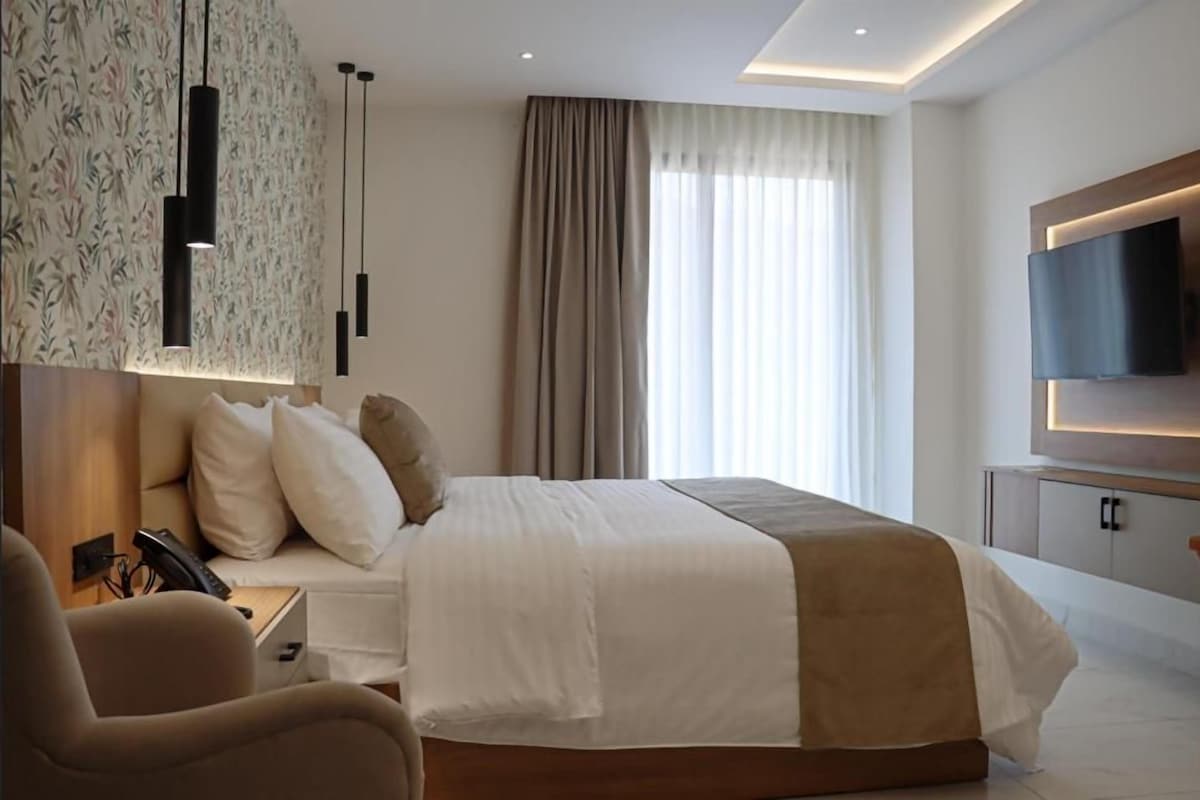 A hotel room with a large bed, a TV mounted on the wall, a desk with a phone, and a chair.