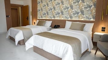 Quarto de hotel com duas camas, cabeceira de madeira, papel de parede floral e luminária moderna.