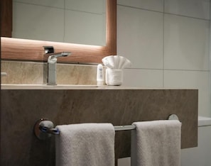 A bathroom with a marble countertop, a towel rack with two towels, a mirror, and a tissue dispenser.