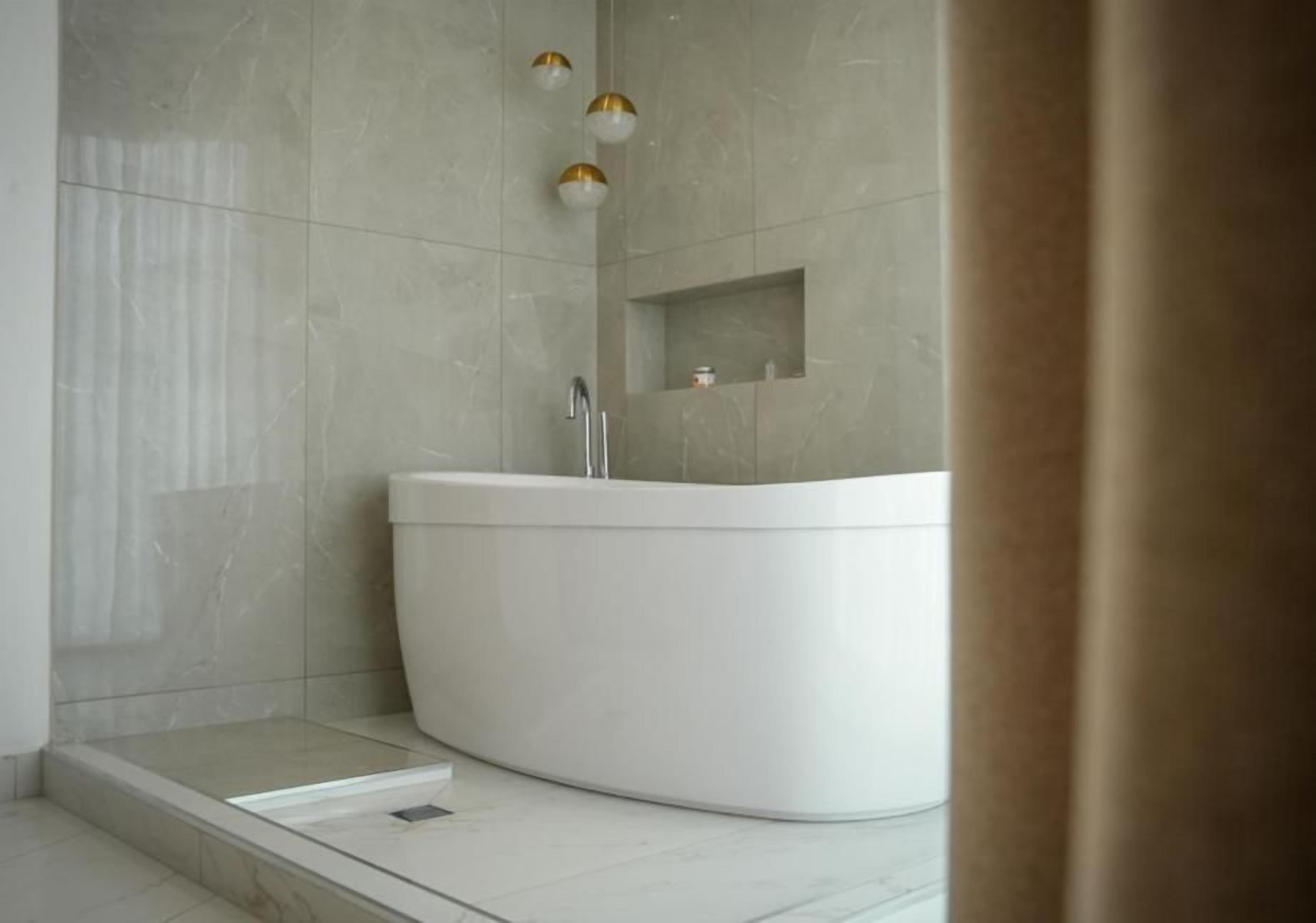 A modern bathroom with a freestanding bathtub, a shower area, and a small shelf with toiletries.